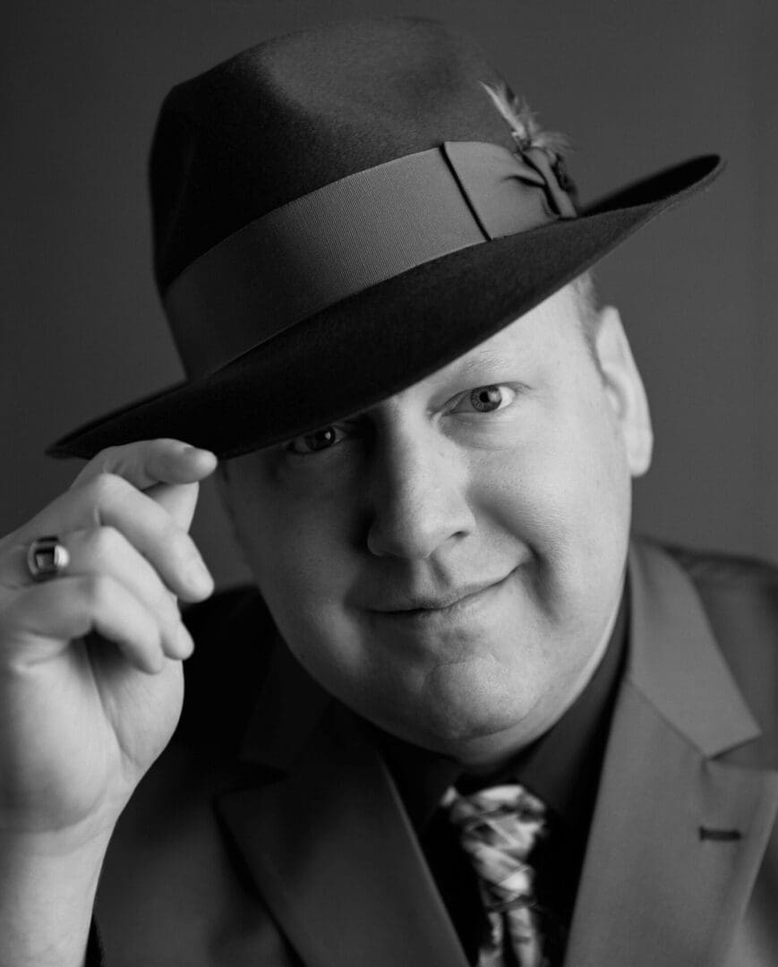 Man wearing suit and hat, smiling confidently.