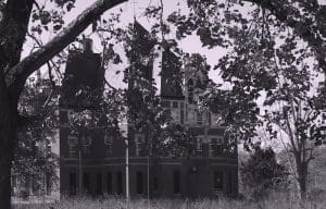 Haunted house behind tree branches, black and white.