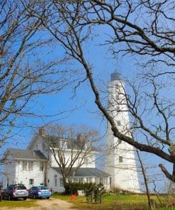 Lighthouse with house and trees in foreground.