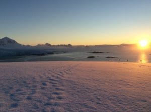 Snowy landscape with sunrise over mountains.
