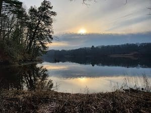 Sunset over calm lake with trees reflected.