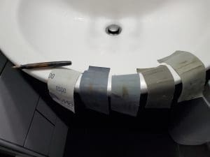 Sandpaper sheets and pen on sink edge.